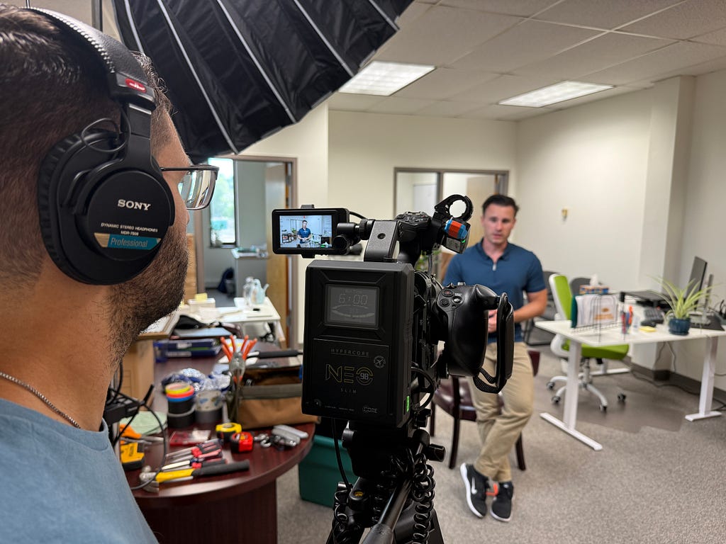A business person speaks directly to camera with an operator looking through the viewfinder.