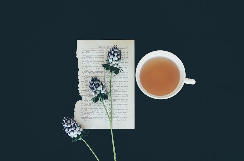 Overhead view of a mug of tea, aa few flowers, and a page of poetry ripped from a book