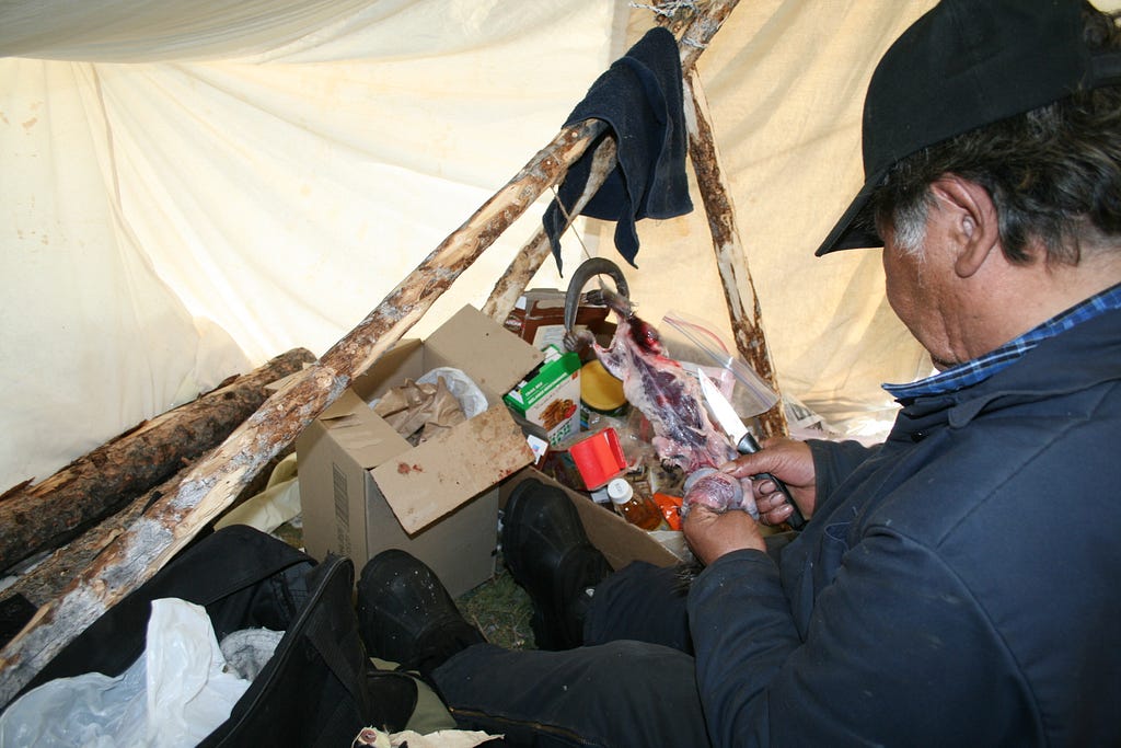 A man in a tent is skinning a small animal.