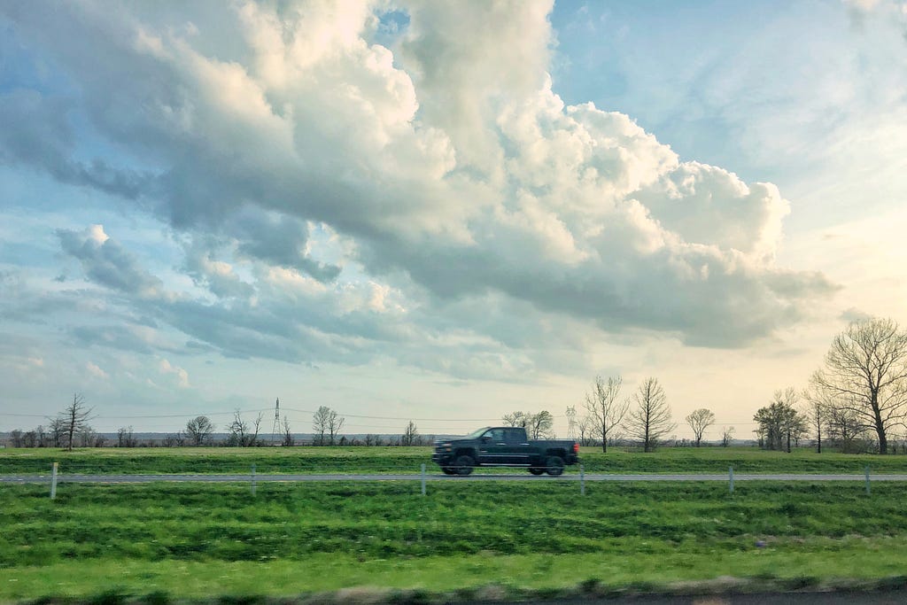 A truck cruises by in western rural Louisianna with fluffy clouds in the sky