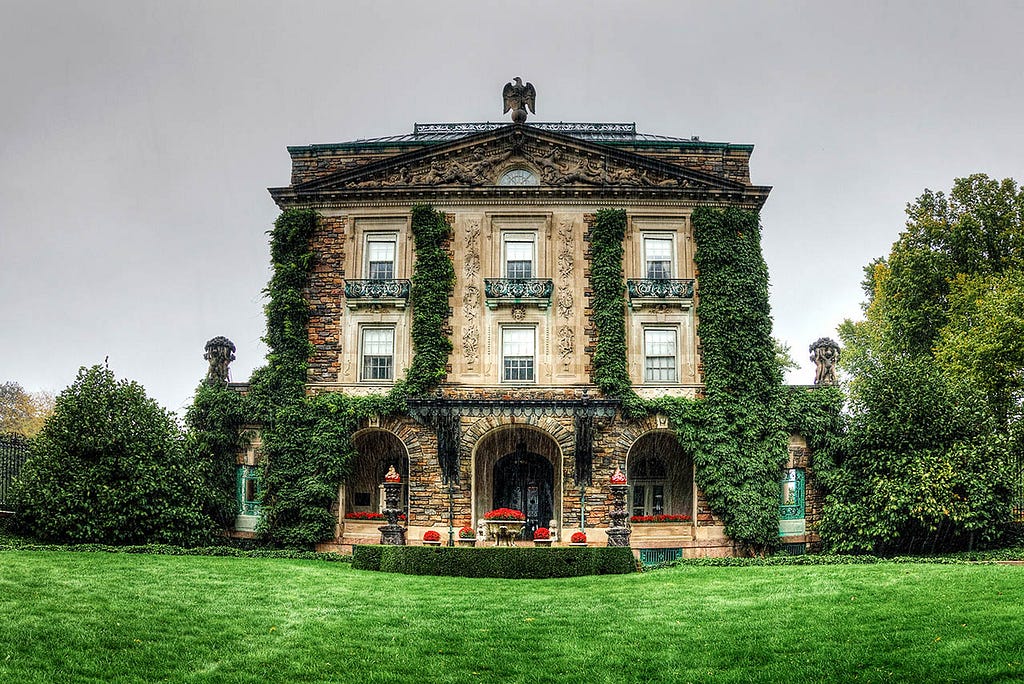 An imposing mansion with a vine-covered exterior. The grand house has many windows and appears to be set amongst trees.