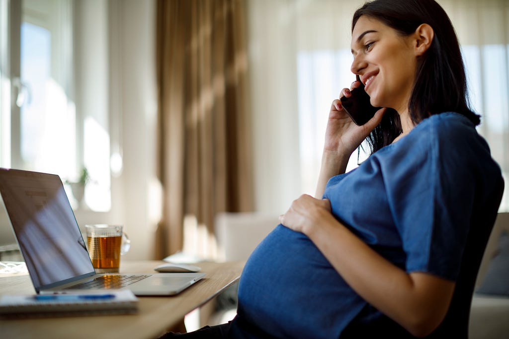 Pregnant woman talking on the phone while working from her home office
