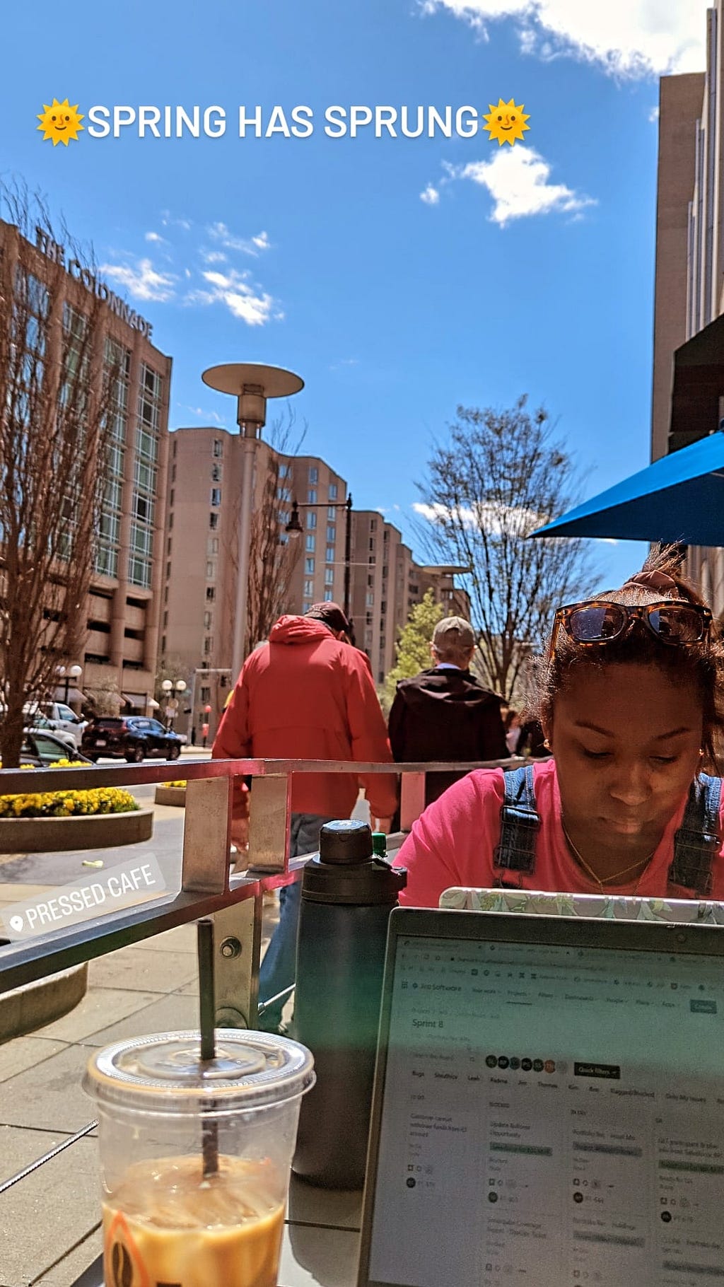 Outside work setup at a cafe with sun shining and blue sky and words “Spring has sprung” written on it