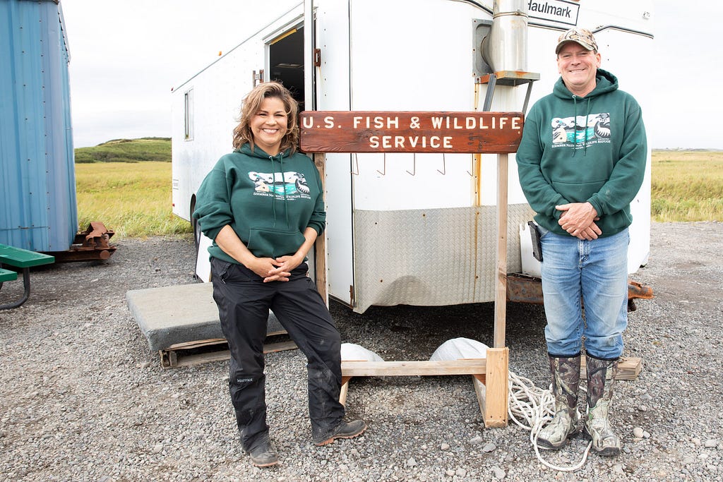 A woman and man stand in front of a U.S. Fish and Wildlife Service sign