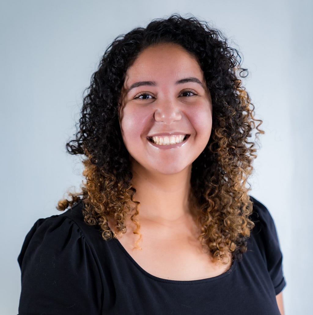 An image of Alaa Mohammed wearing a black blouse smiling with a light background