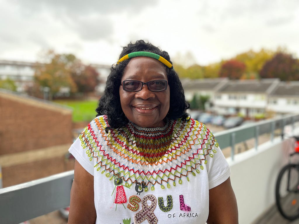 Thabani is an older woman smiling at the camera while stood on a balcony.