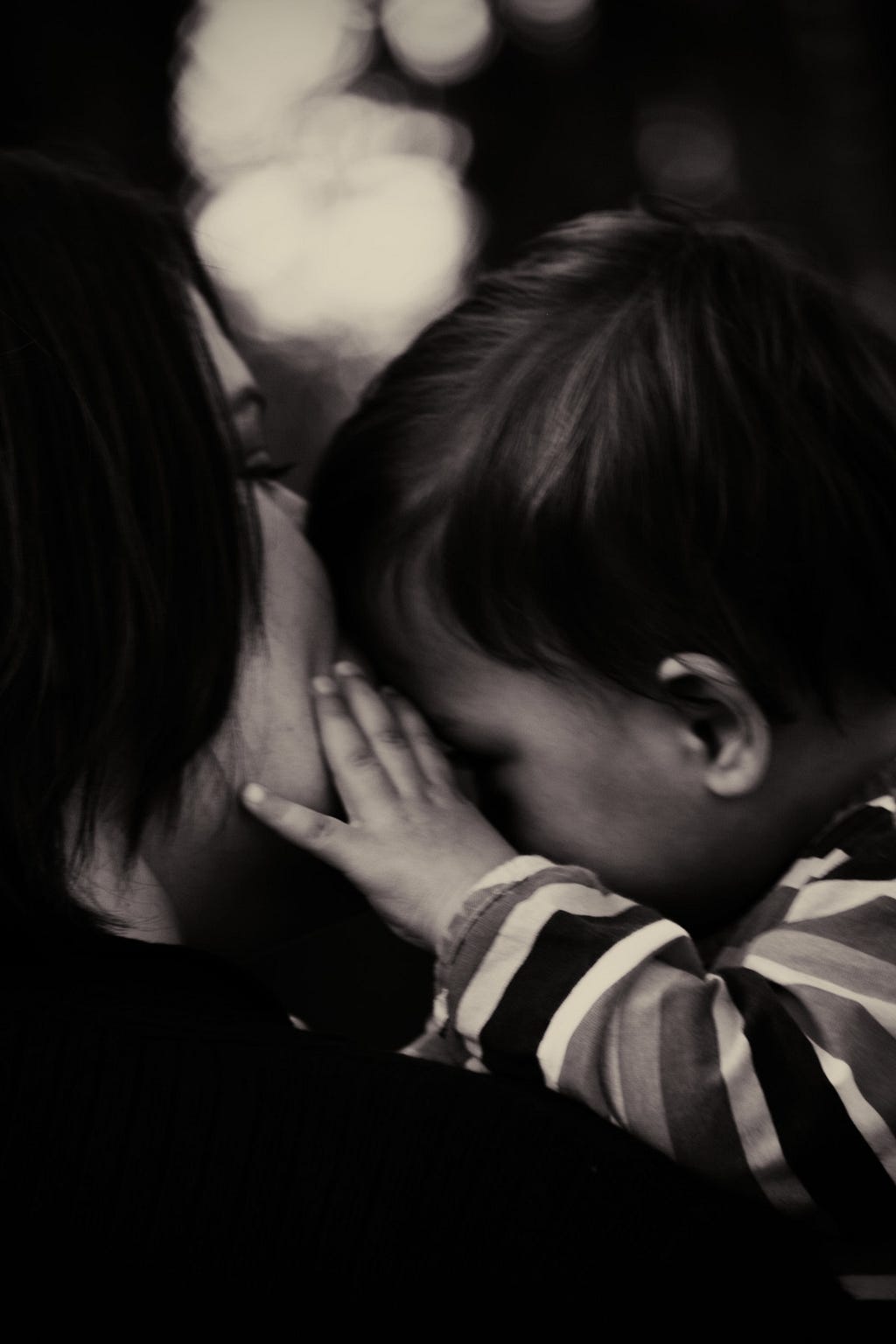 A black and white close up photo of a woman kissing a young child on the forehead while the child’s hand rests on the woman’s cheek