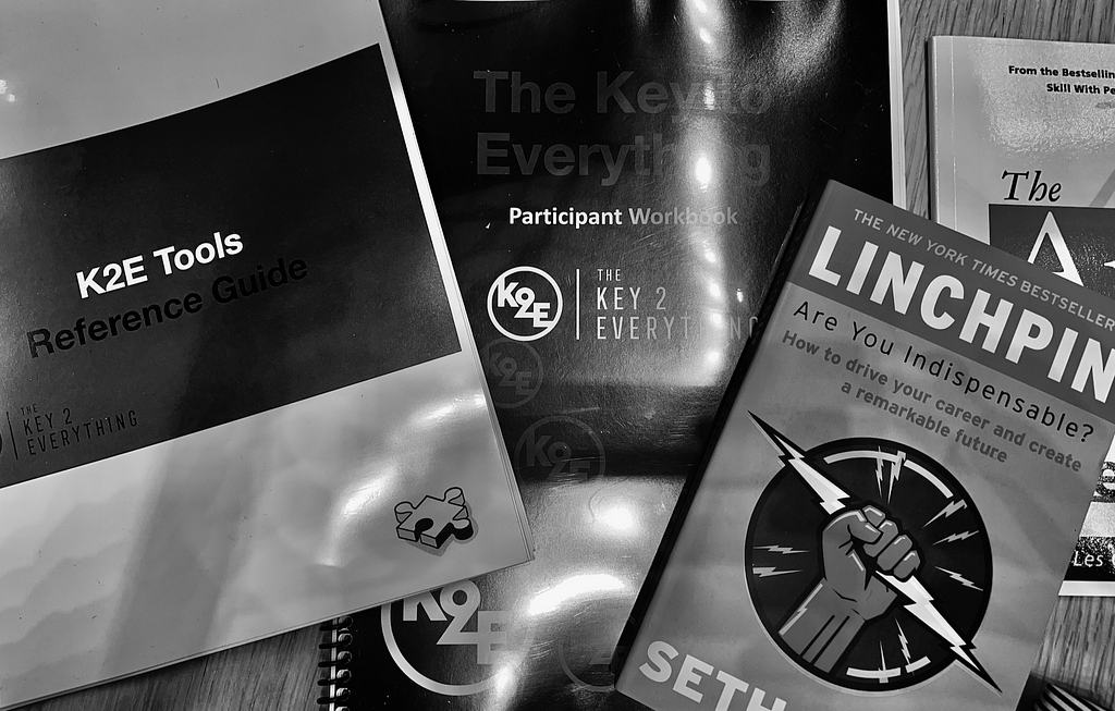 Key 2 Everything course materials laid out on a desk, including a a workbook, a resources guide, Linchpin book by Seth Godin, and the the Art of Dealing with People book.