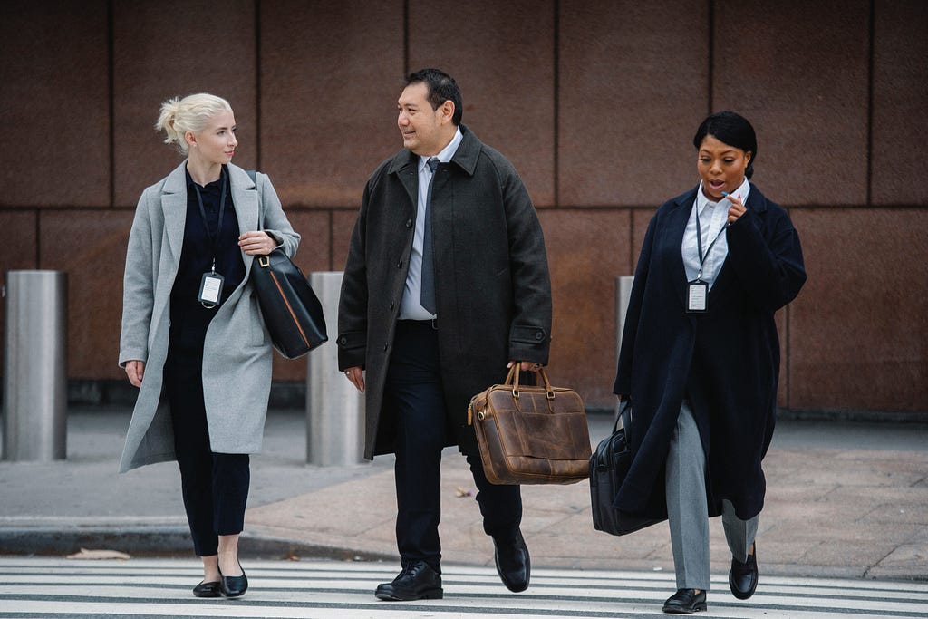 Three business colleagues wearing coats walking across a crosswalk.