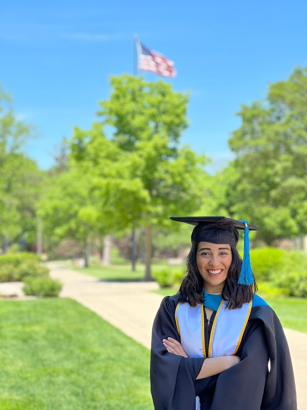 Marla standing outside in front of trees posing in her graduation robes.