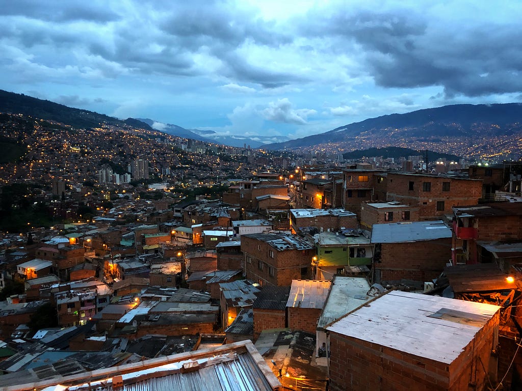 Medellin, Colombia at sunset in Comuna 13 on the Graffiti Tour with city lights glowing on for night time with a cloudy sky