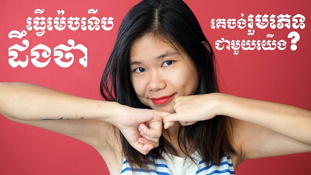A women interlocks her pinky’s together. Behind her are Khmer words discussing affirmative consent.