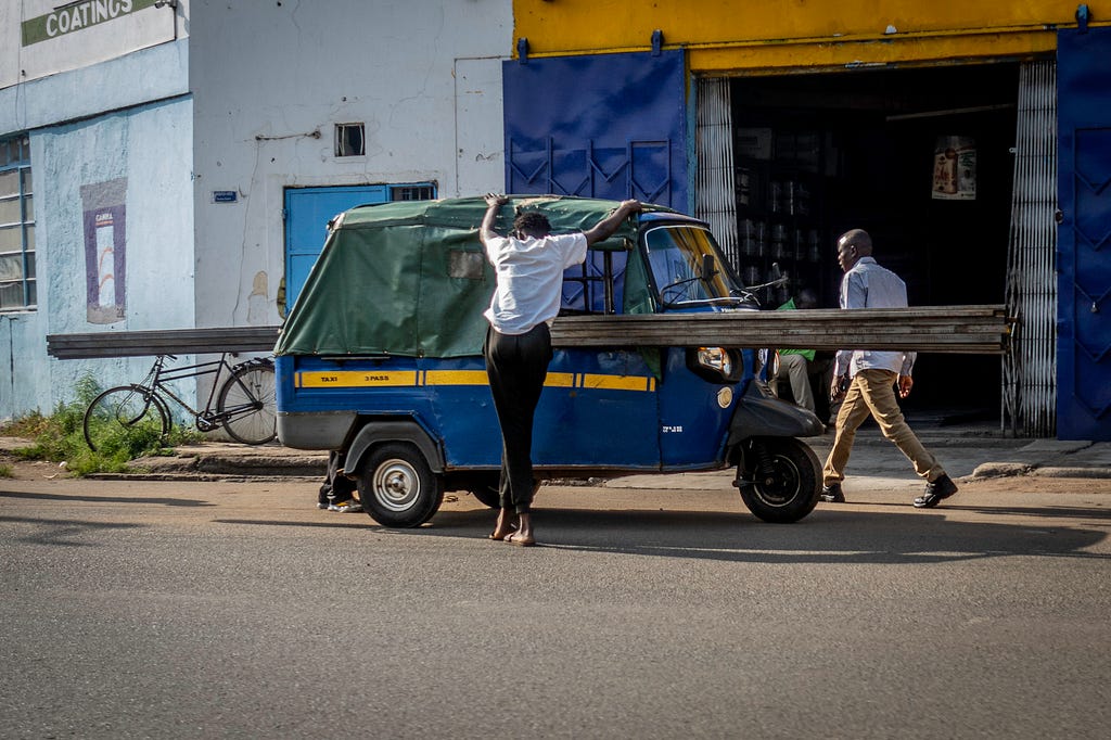 A blue and yellow tuk tuk parked on the road and loaded with beams.