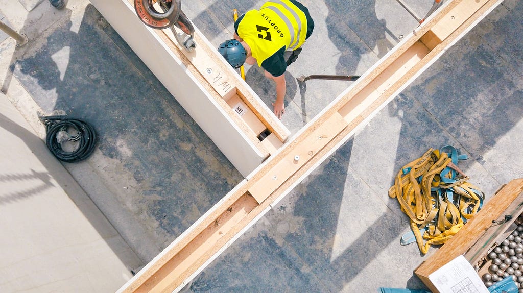 High-view walls on construction site. Men in yellow vest wearing protective gear bending down.