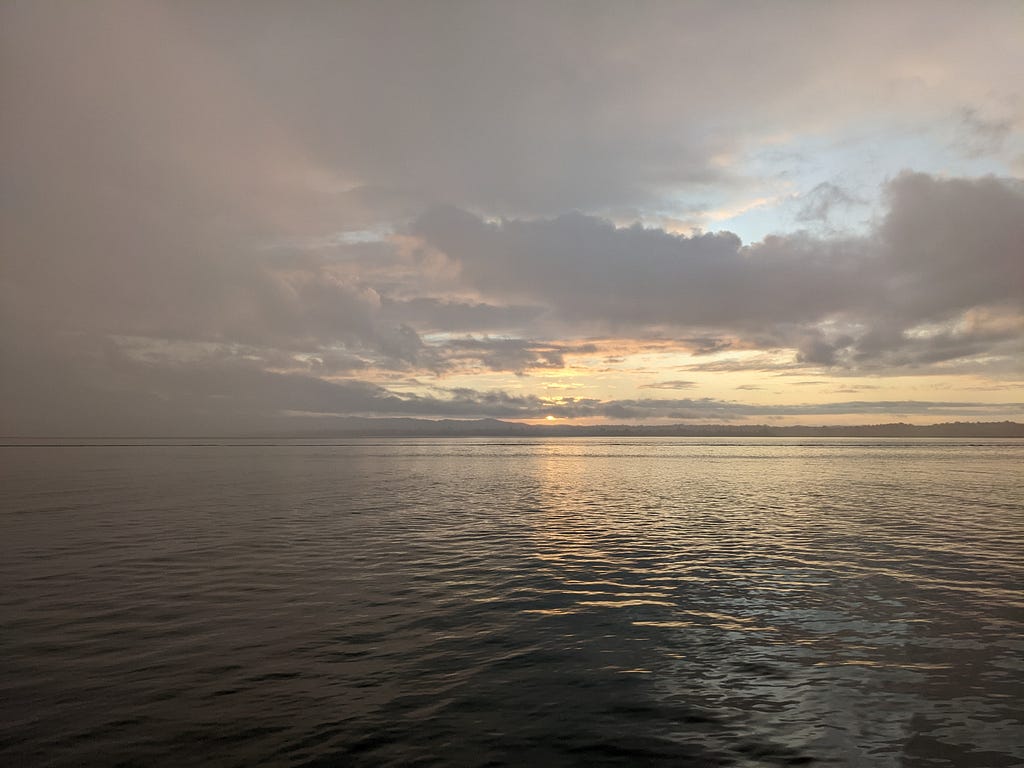 Pastel coloured sunset in a cloud-filled sky over a still grey ocean