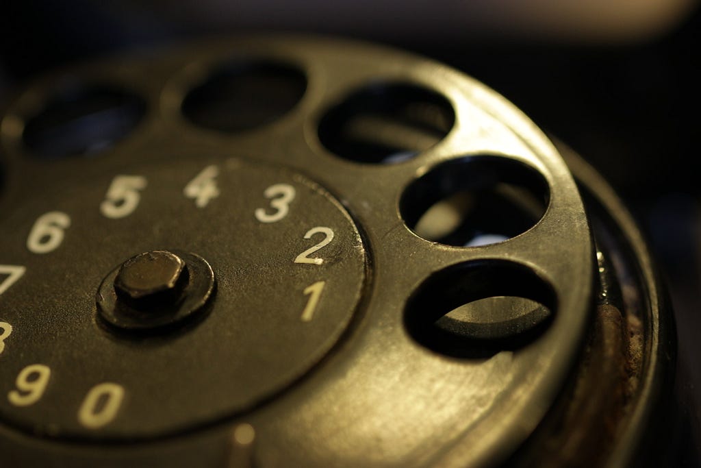a rotary telephone dial made out of black metal, seems ancient and heavily used