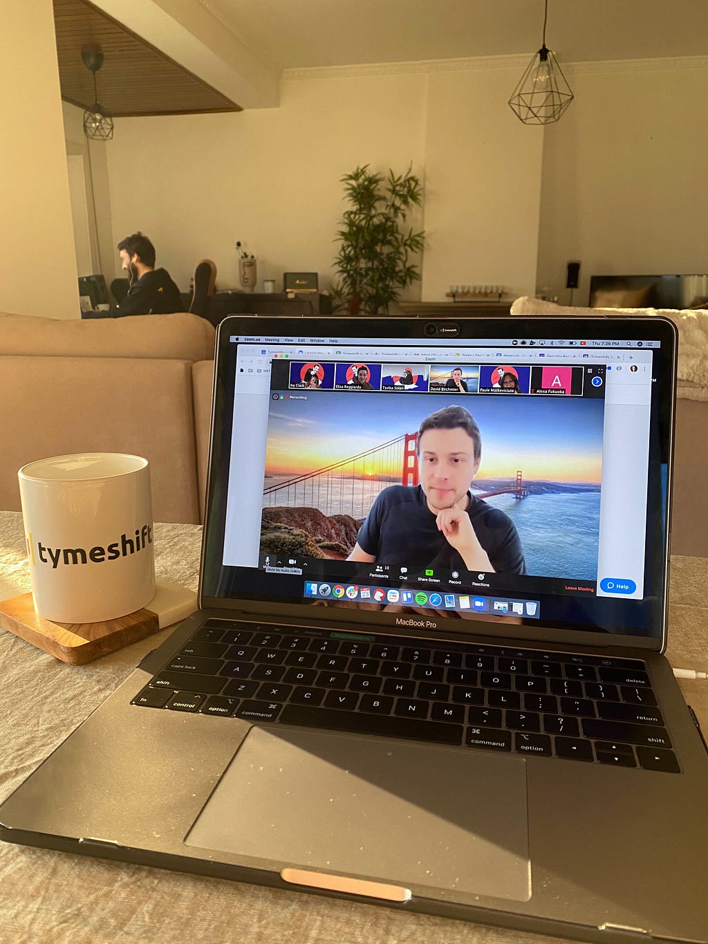 A mug and laptop sit on a table with a Zoom meeting showing on the laptop screen.
