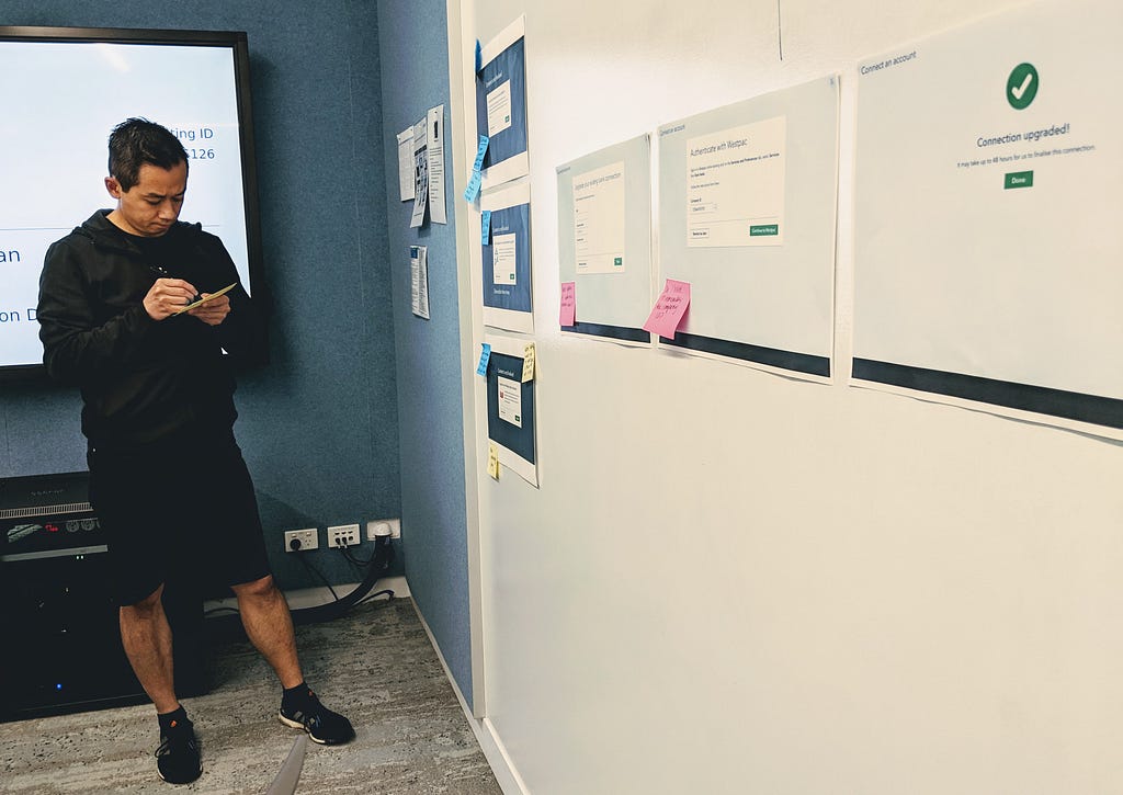 A developer is making notes next to printed design user journey on a wall