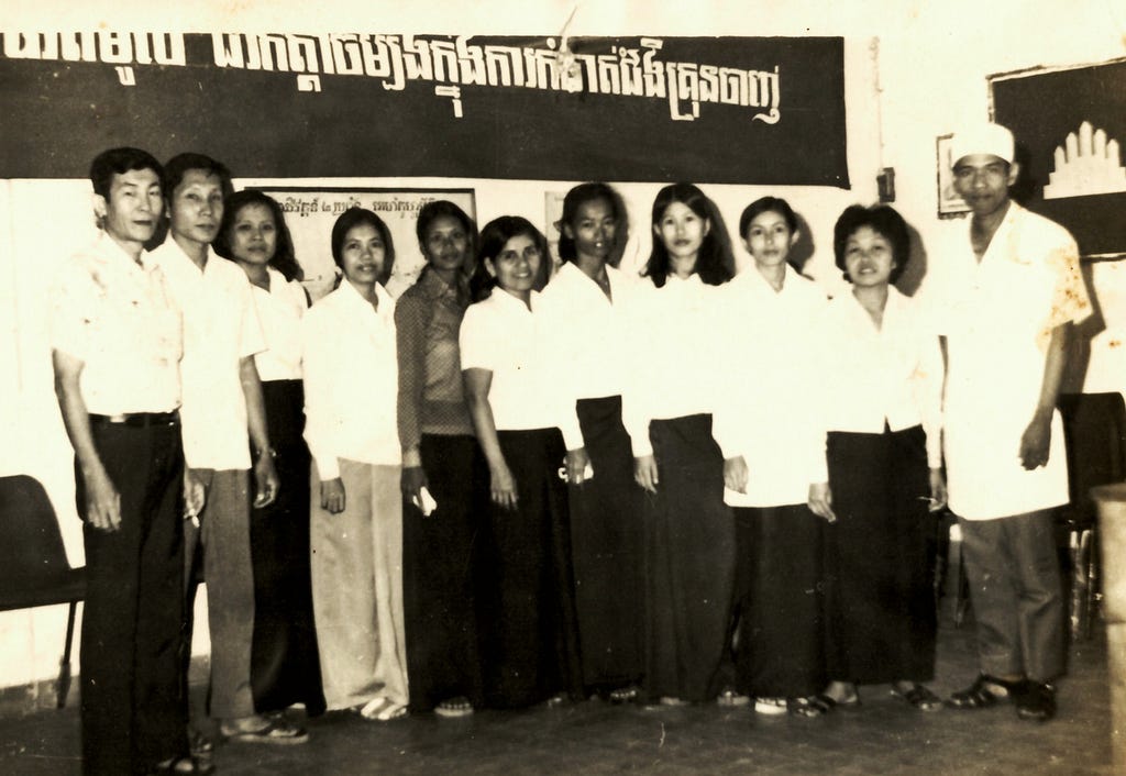 A group of people line up for a group photo. The image is black and white and from the 1980s.