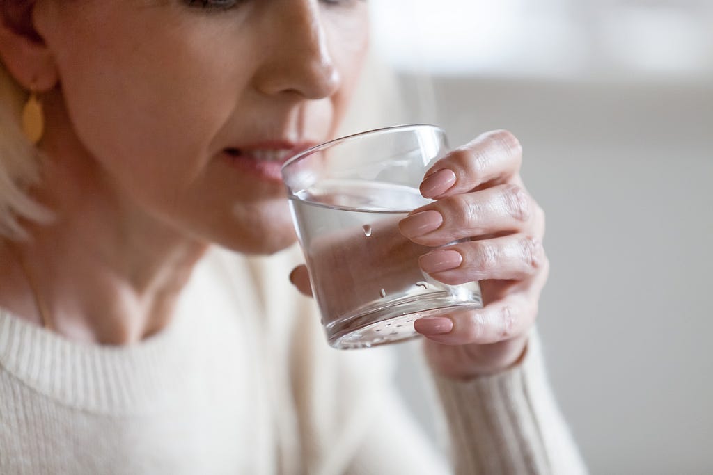 Elderly woman holding glass feeling thirsty or dehydrated, senior lady drinking water to prevent dehydration