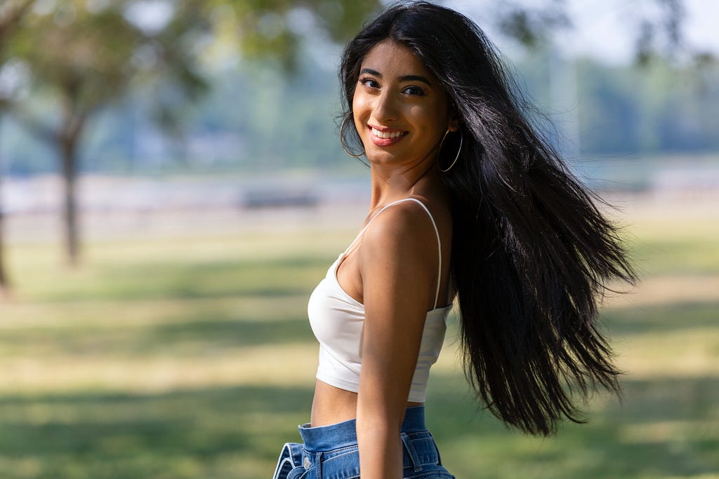 A woman in a white top crop is smiling while looking at the camera. Photo by Jeff Denlea from Pexels.