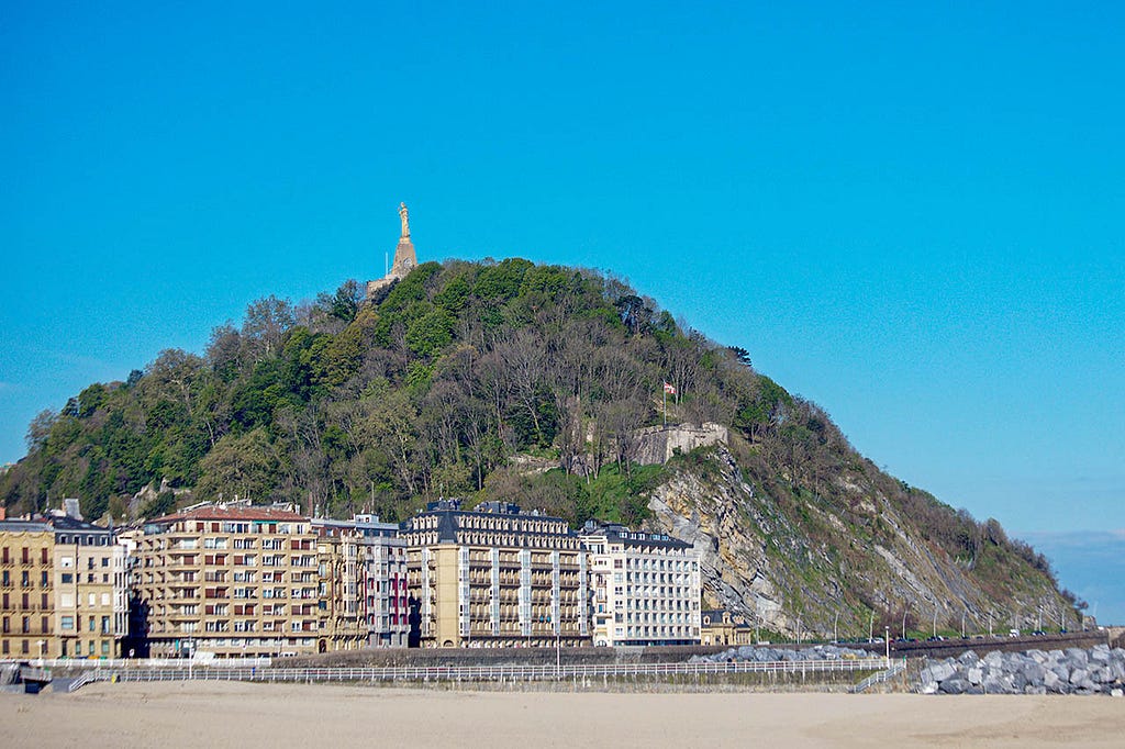 a small group of multi-story apartments in front of a hill with a christ statue