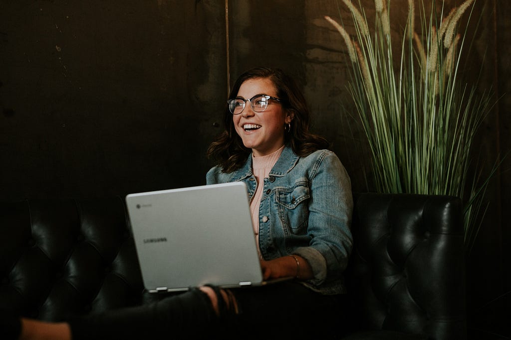 A female user smiling on a leather couch and testing a digital product on her laptop.