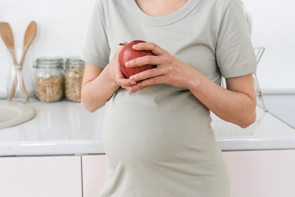 Crop pregnant woman with apple.