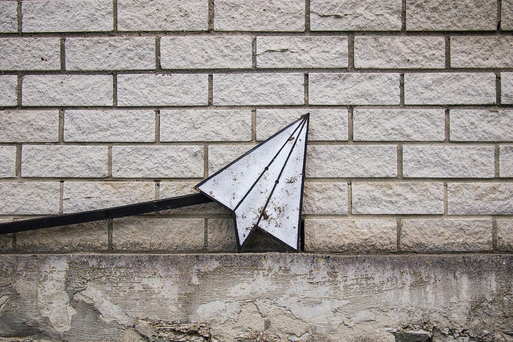 White metal paper plane against a white brick wall.