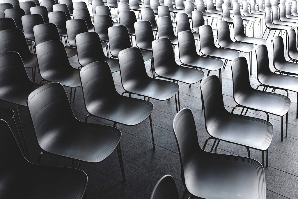 Many rows of black chairs behind each other.