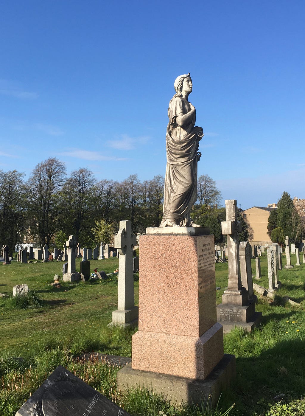 The dirty grey-white statue of a woman in a graveyard from an angle where you can see her face, with blue sky behind