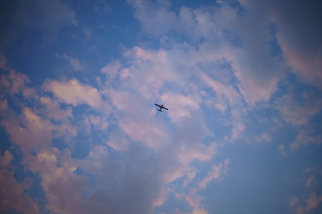 An airplane flying low, behind a fluffy fragmented cloud refracts the orange of the sunset making a contrast of the intense blue in the sky. Un aeroplano volando, detrás una nube acolchonada pero fragmentada refracta la luz del atardecer contrastando con el intenso azul en el cielo.