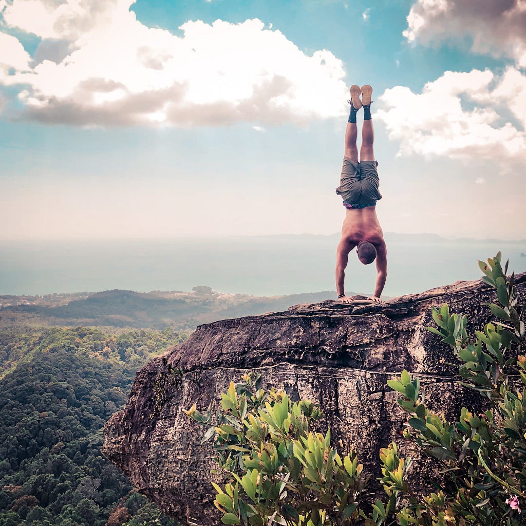 How to instantly improve your handstand header image. The author doing a handstand on the edge of a cliff in Krabi, Thailand.