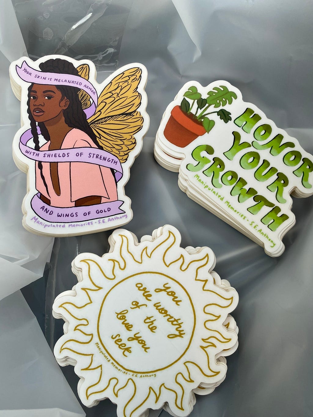 A group of different sticker designs. The designs feature a sun, a potted plant, and a young woman with wings.