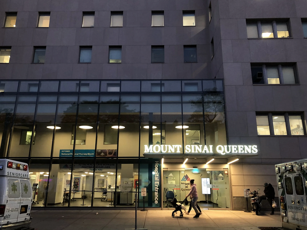 A photograph of Mount Sinai Queens in Astoria at dusk, framed by two ambulances