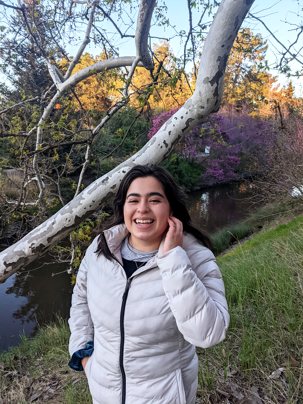 Dani Solis stands on a grassy hill by a tree, smiling.