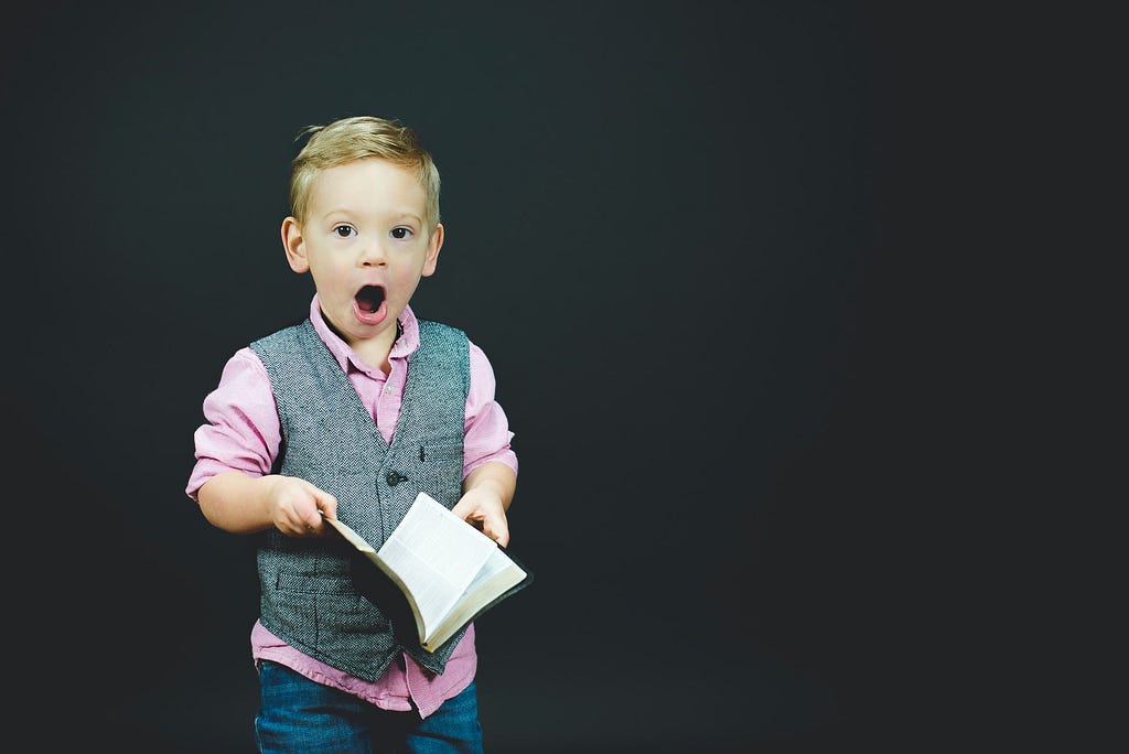 child holding a book with eyes and mouth open wide with surprise