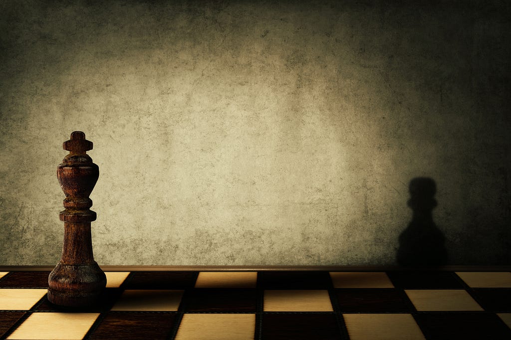 A darkly lit chess board where the King chess piece casts a shadow on the only other piece, which is a pawn.