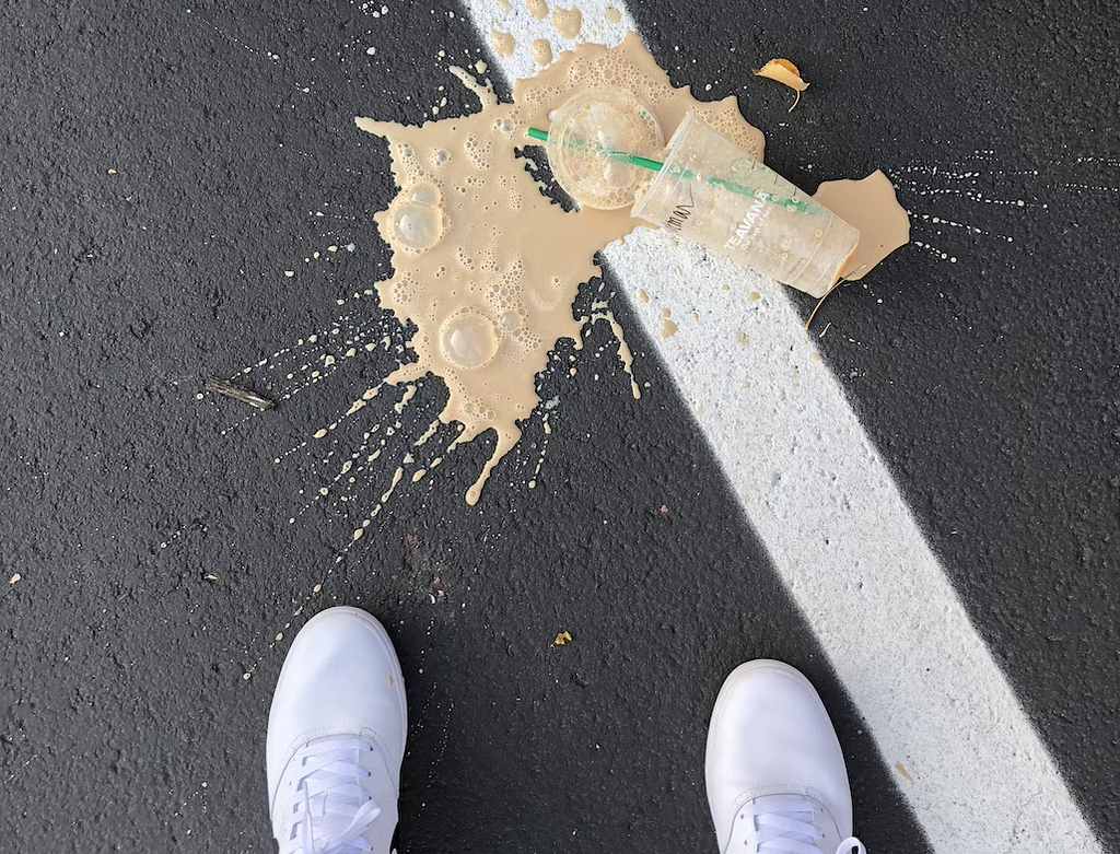 Coffee spilled on the ground next to white shoes.