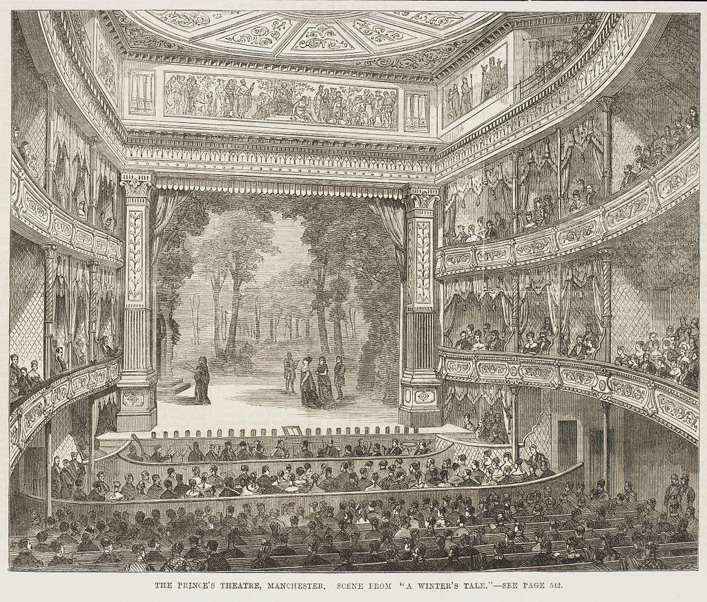 Elaborately decorated theatre interior with actors on stage, orchestra pit and a full house including stalls and balconies.