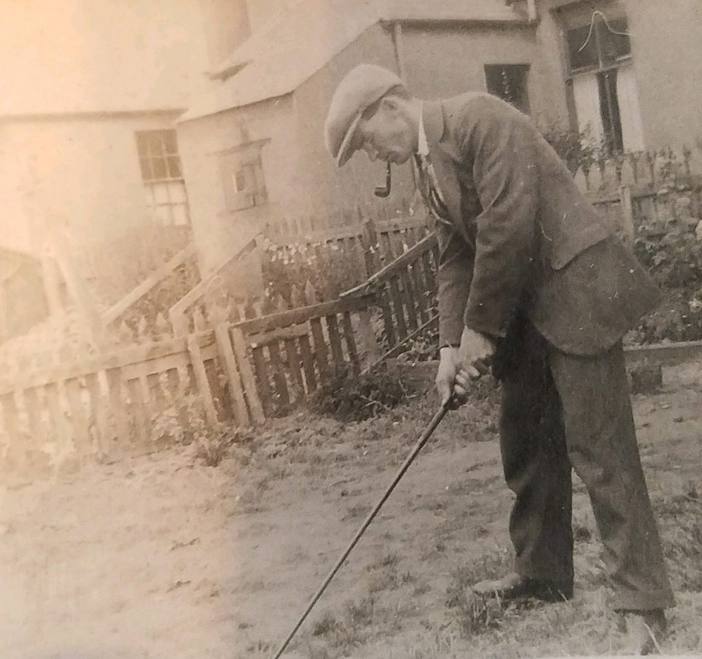 A photo of Arthur Ross addressing a golf ball in the streets of Carnoustie, Scotland. He’s in a suit, has a derby hat on, with a pipe in his mouth. Photo from the family archives, late 1930's. Photo by author.