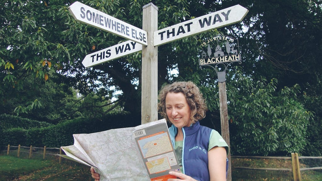 A woman is looking at a map in front of a wayfinding sign with points to three directions: this way, that way, somewhere else.
