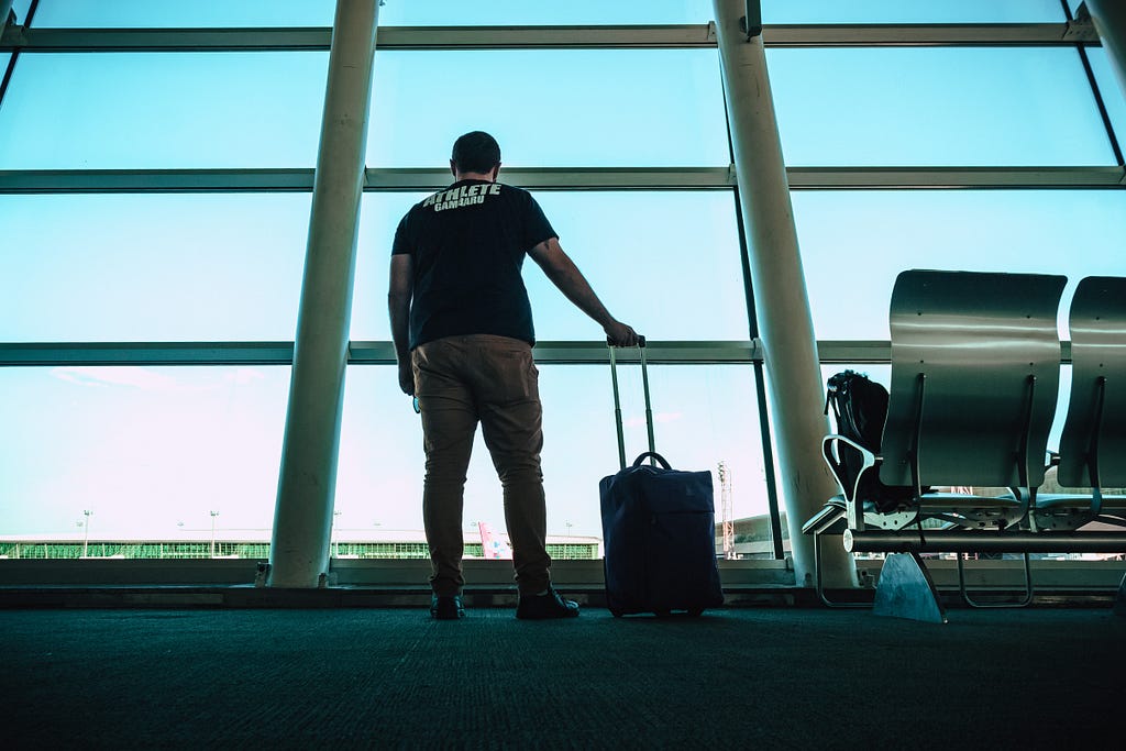 A man stands with his carry-on looking out at the tarmac of the airport