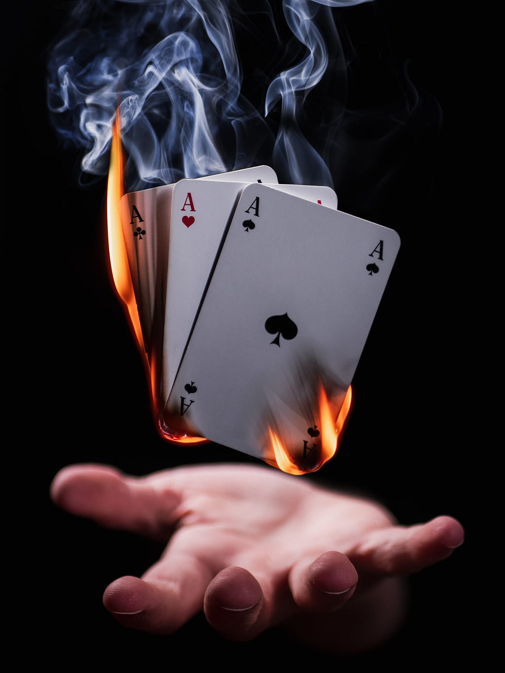 A white hand outstretched with playing cards hovering above it. The cards are on fire.