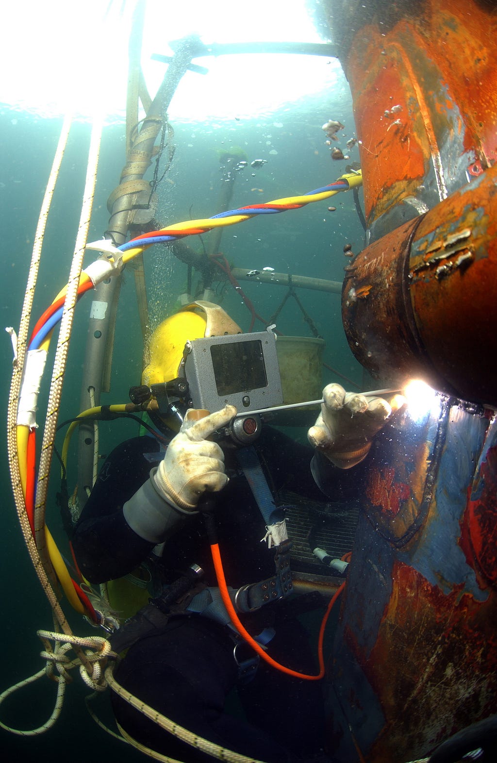 A diver welds a part onto the underwater bow of the ship.