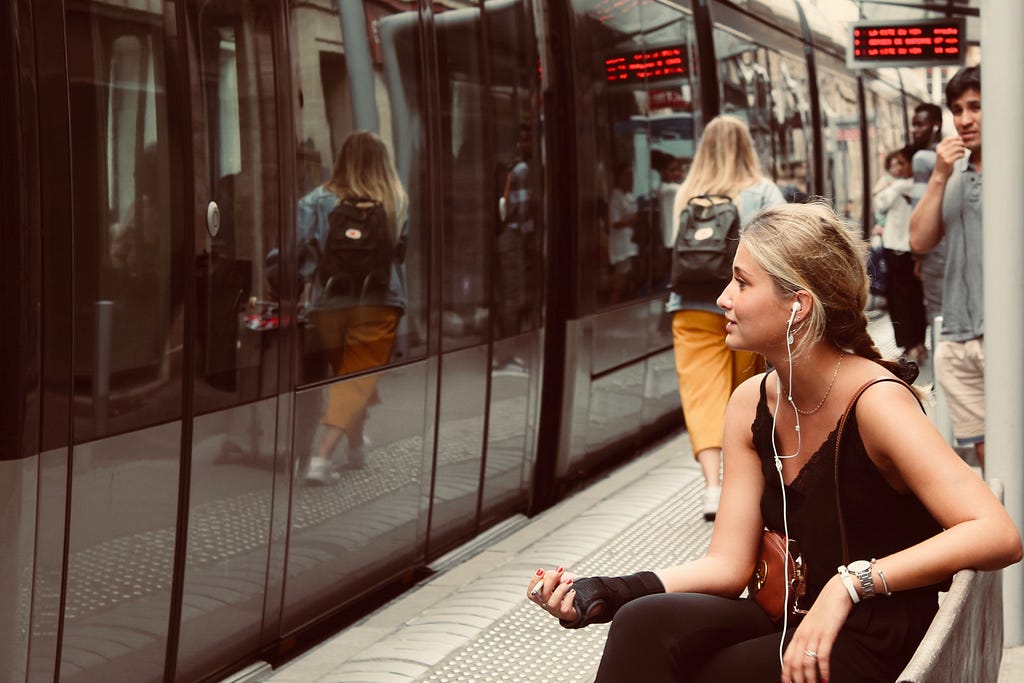 A girl sitting on a subway station with earphones in her ears.