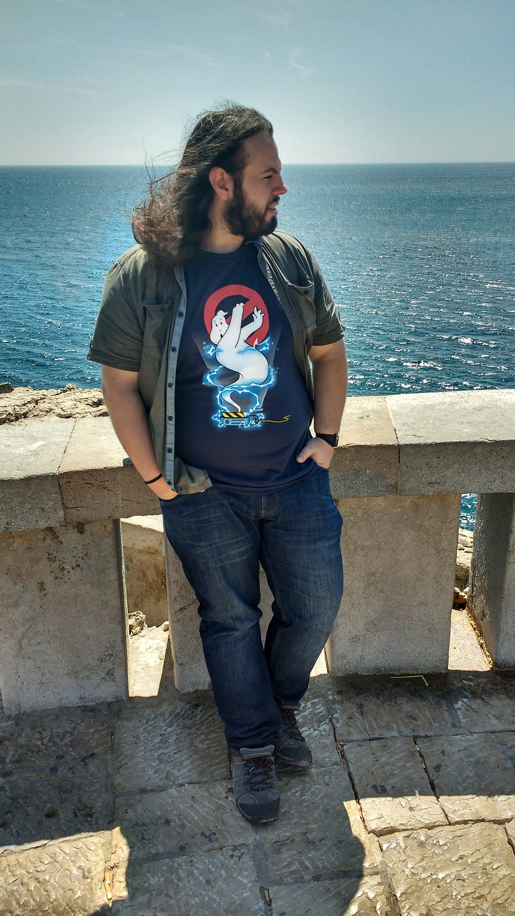 A man wearing a ghostbusters shirt stands in front of blue water.