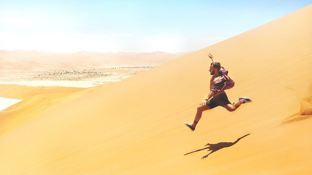 man running swiftly down a large sand dune