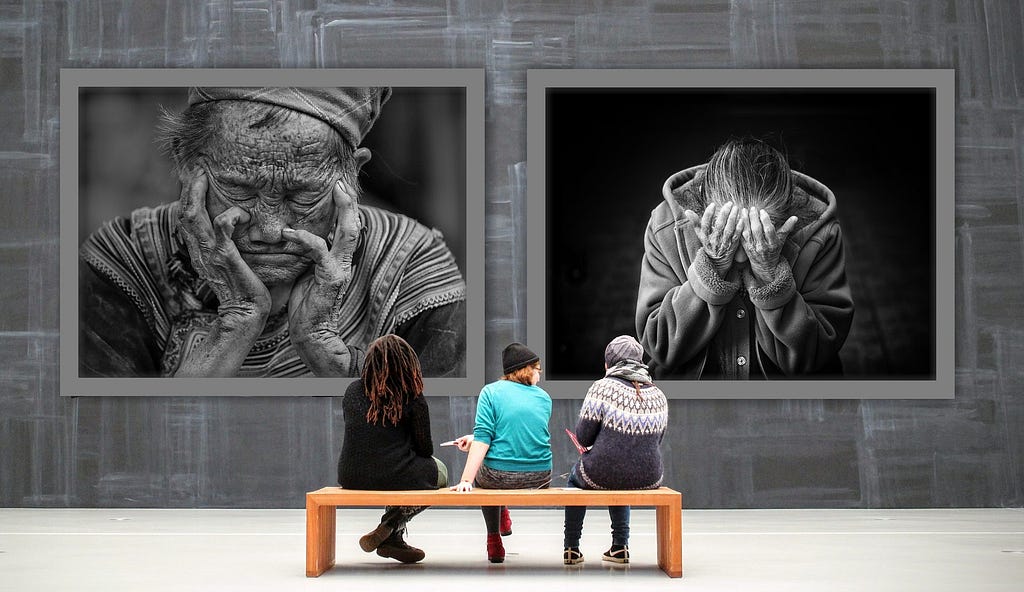 Three people sit on a bench looking at black and white portraits on a wall.