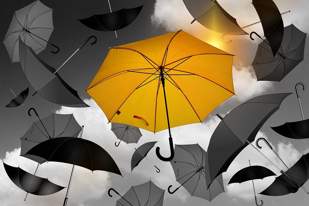 Black and white image of umbrellas floating in the sky. The center umbrella is yellow.